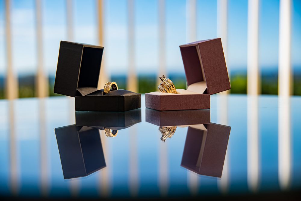 Two open jewelry boxes with rings are reflected on a glossy surface against a blurred blue and white background.