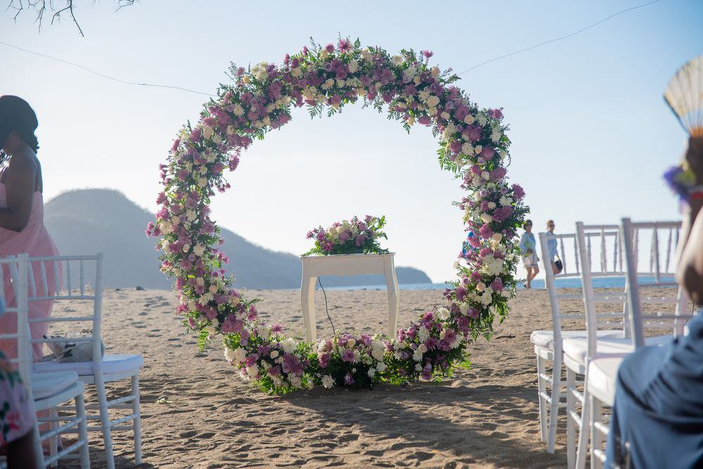 A series of floral arches line a beachfront wedding ceremony setup with white chairs and ocean views.