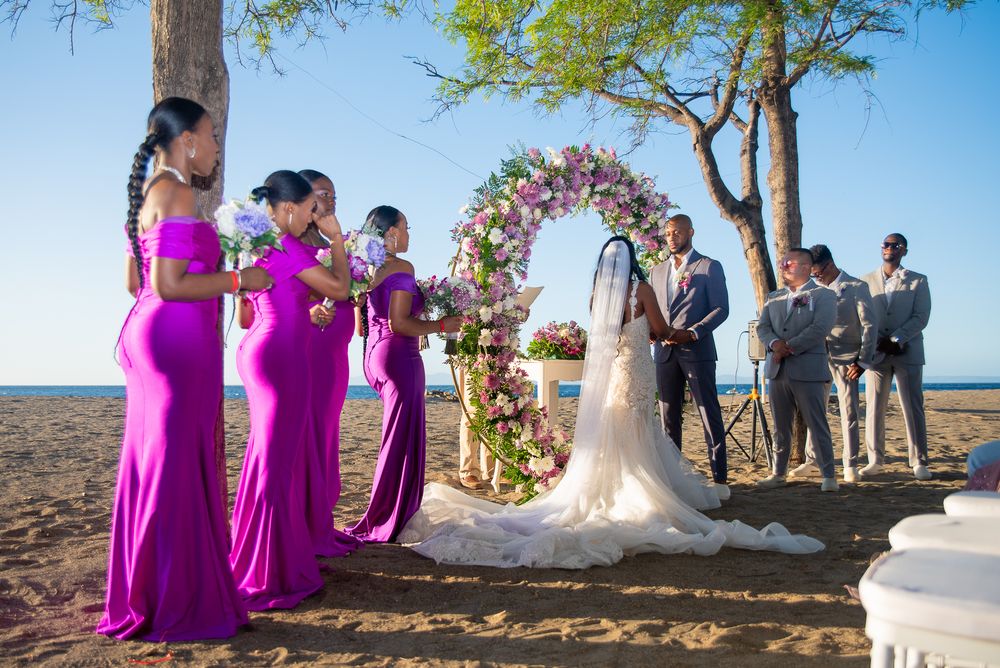 Wedding party in vibrant purple dresses poses outdoors against a scenic backdrop at sunset.