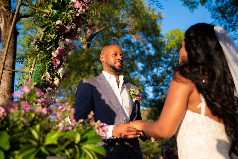 A wedding ceremony takes place outdoors with flowering trees and greenery creating a romantic natural backdrop.