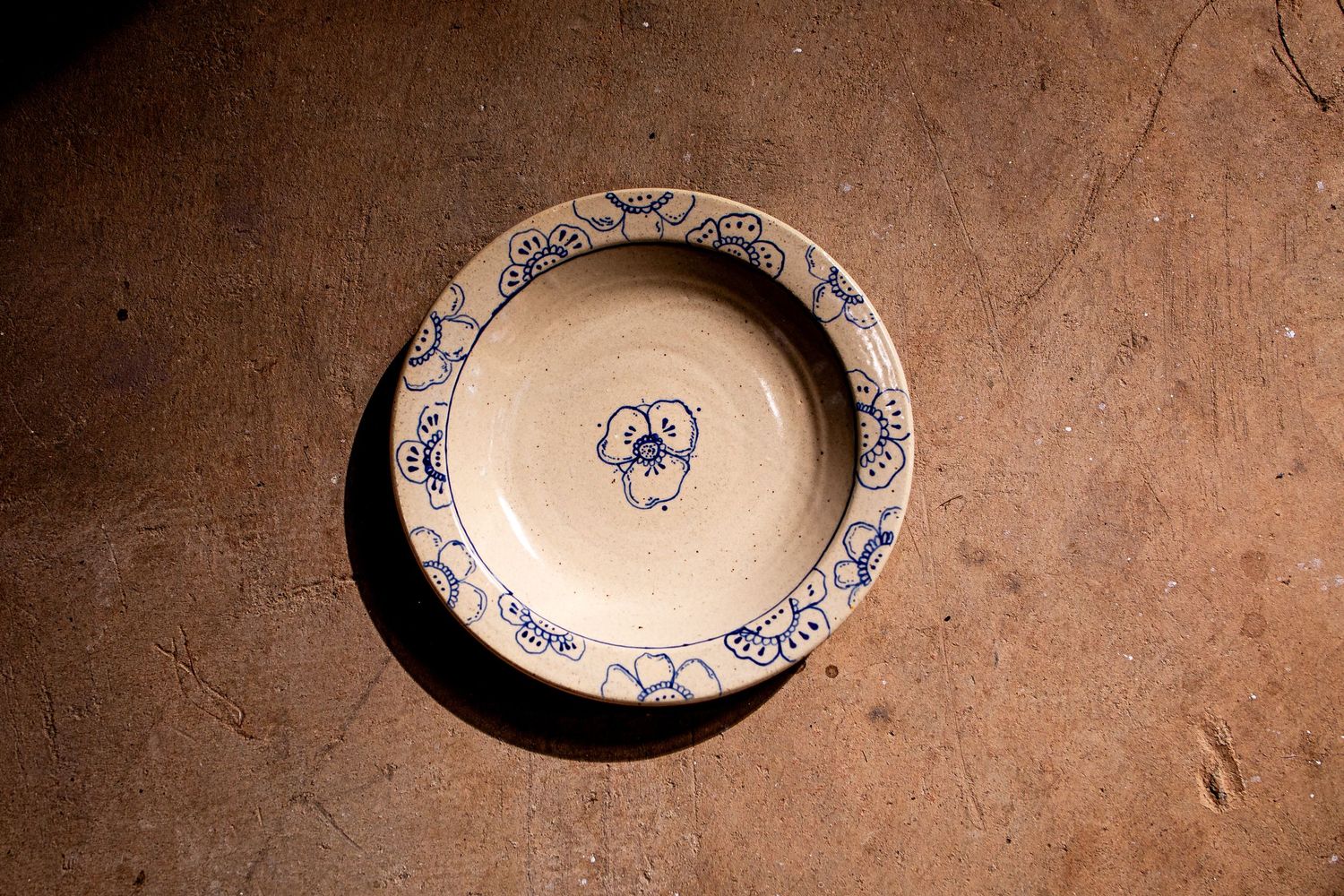 Vintage ceramic bowl with blue floral motifs and pansy center design on rustic terracotta surface.
