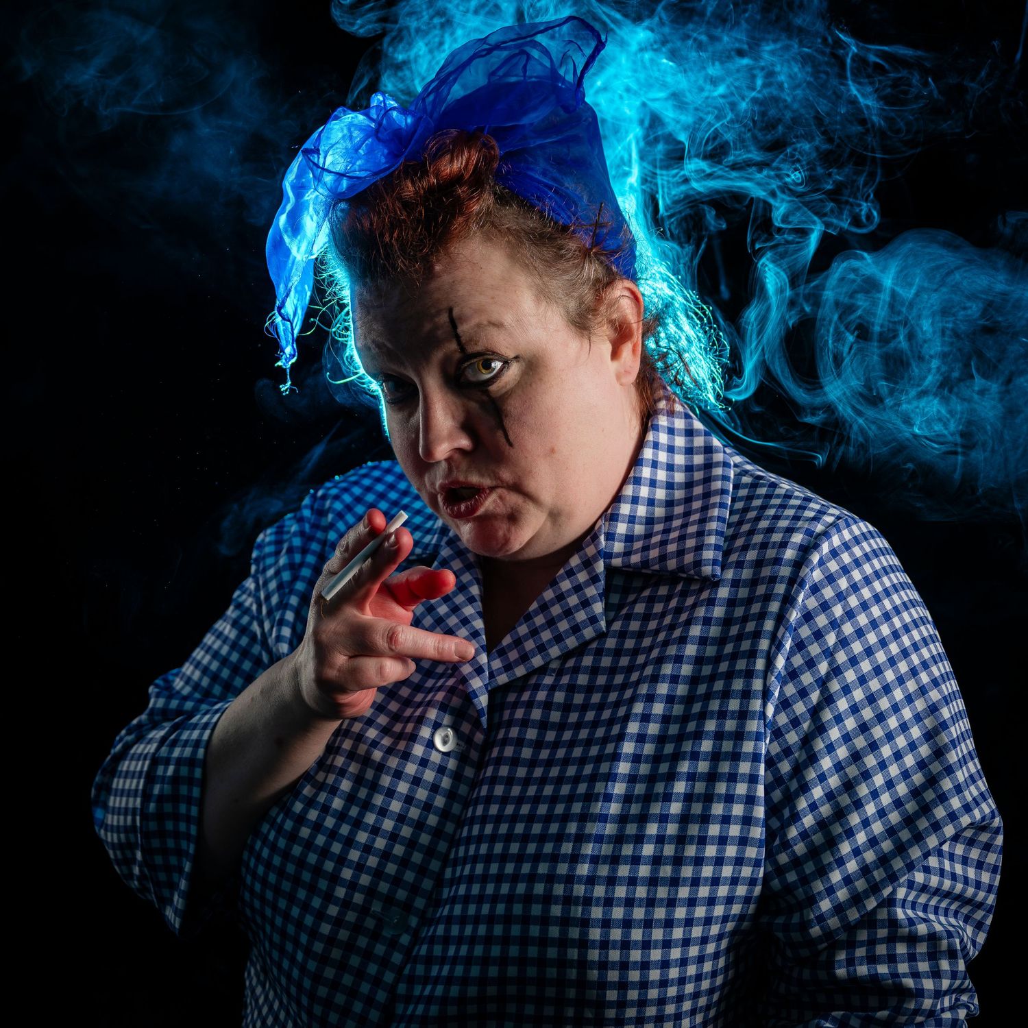 Woman in blue checkered shirt with dramatic blue smoke swirling around her head against dark background.