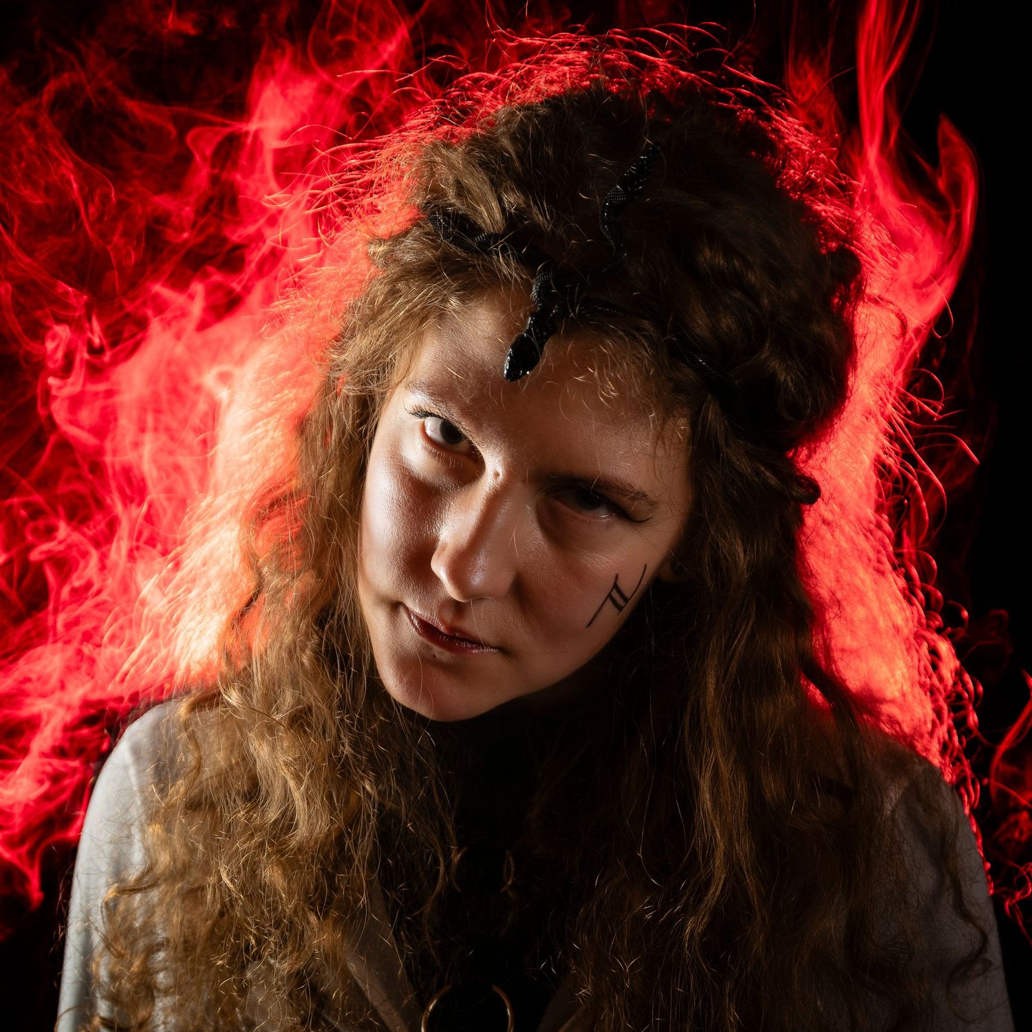 Young woman with curly hair posed against dramatic red flame background in dark, moody portrait photography.