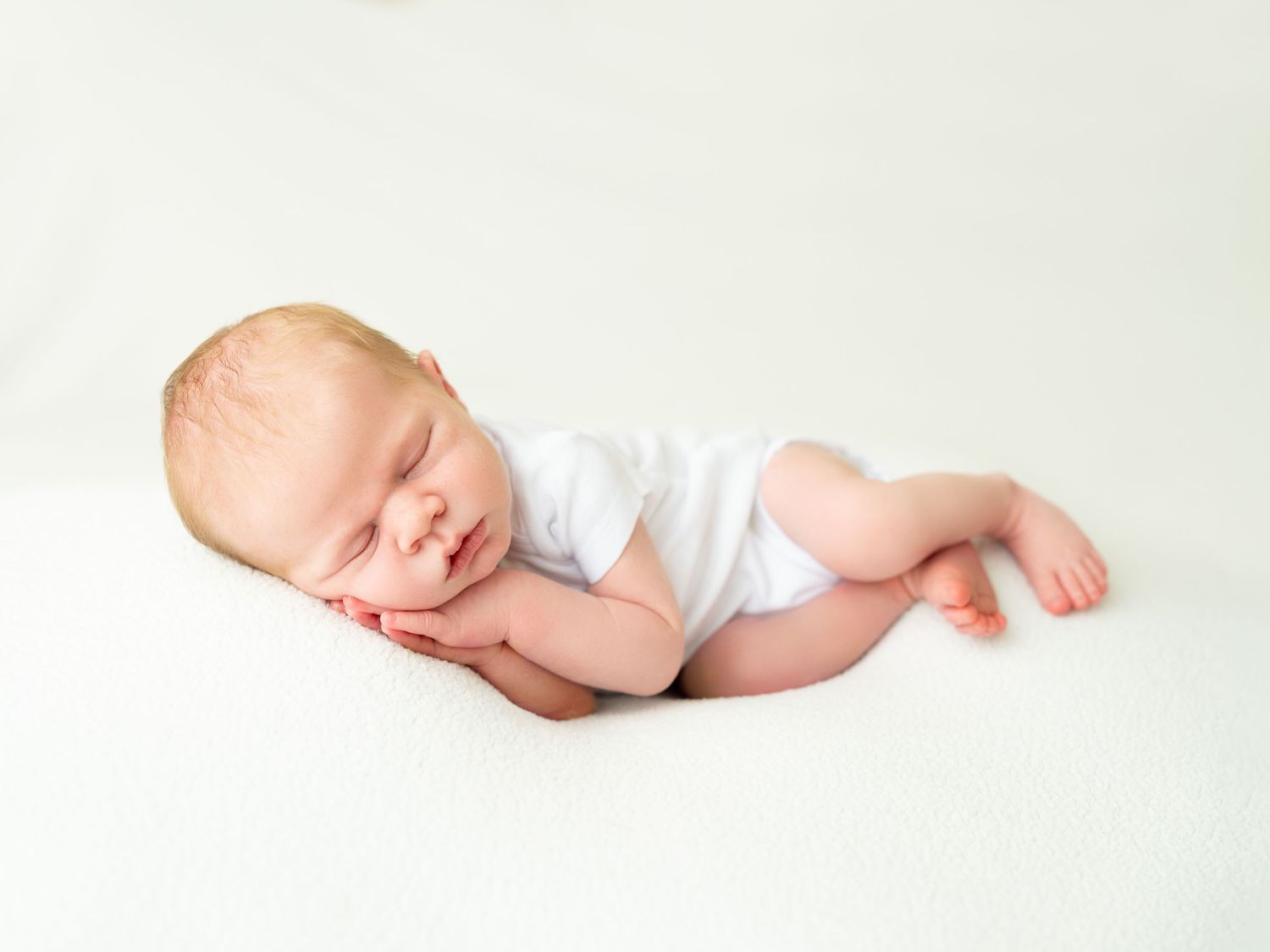 Peaceful newborn baby sleeping on white blanket wearing white onesie, perfect newborn photography portrait.