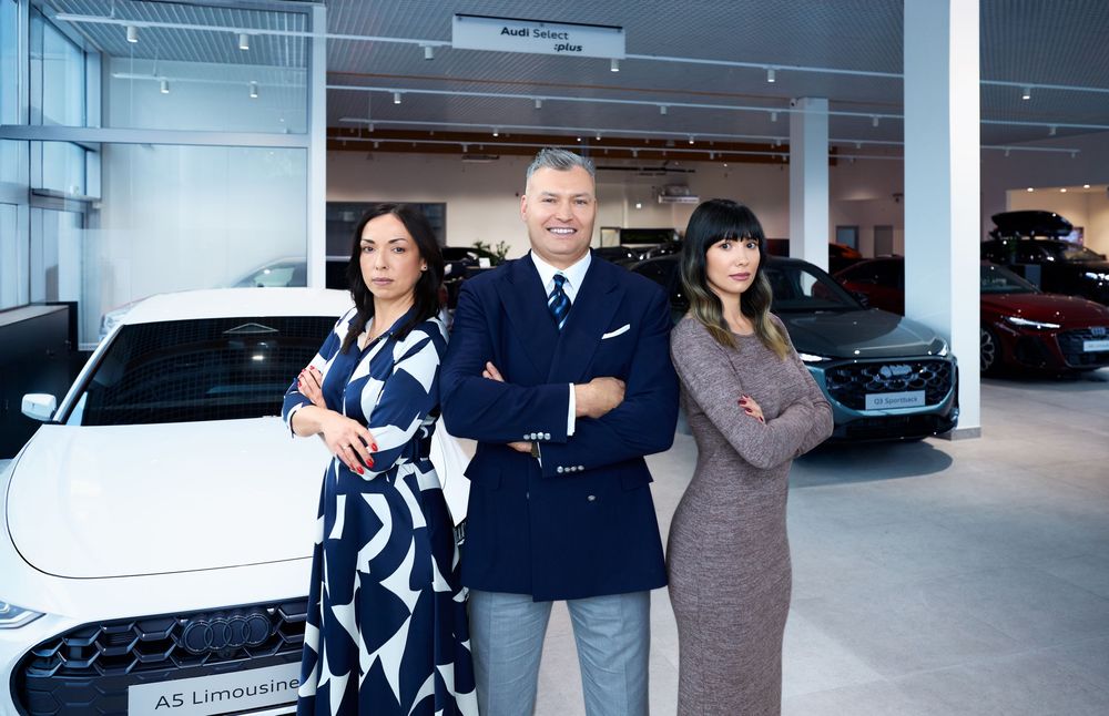 Three car dealership professionals posing confidently in a modern Audi showroom with luxury vehicles on display.