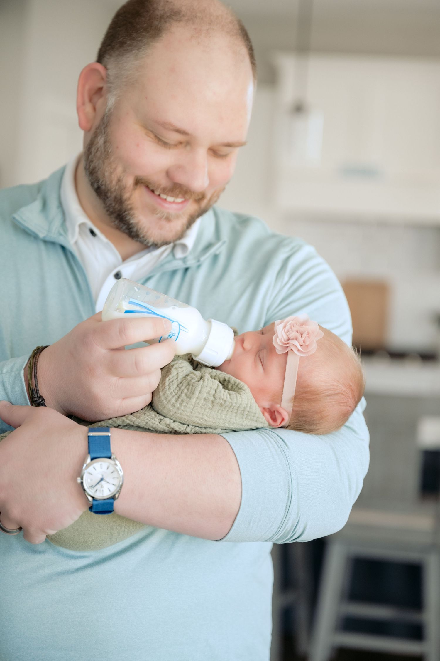dad is smiling while feeding newborn baby during an in home newborn lifestyle session in lake elmo, mn