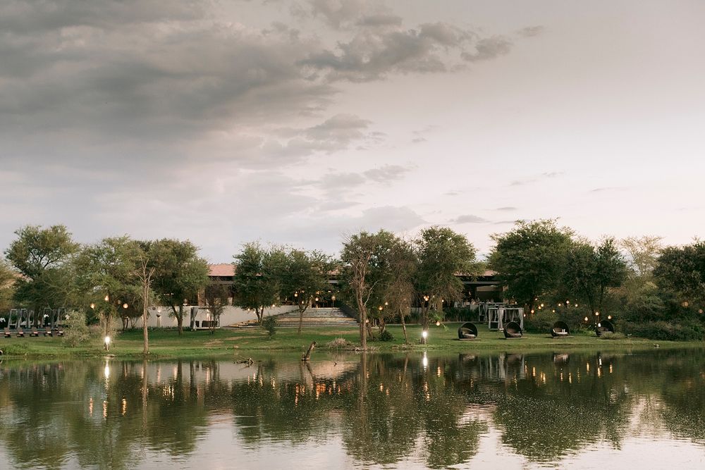 Serene golf course pond reflecting trees and warm string lights at dusk under dramatic cloudy sky.