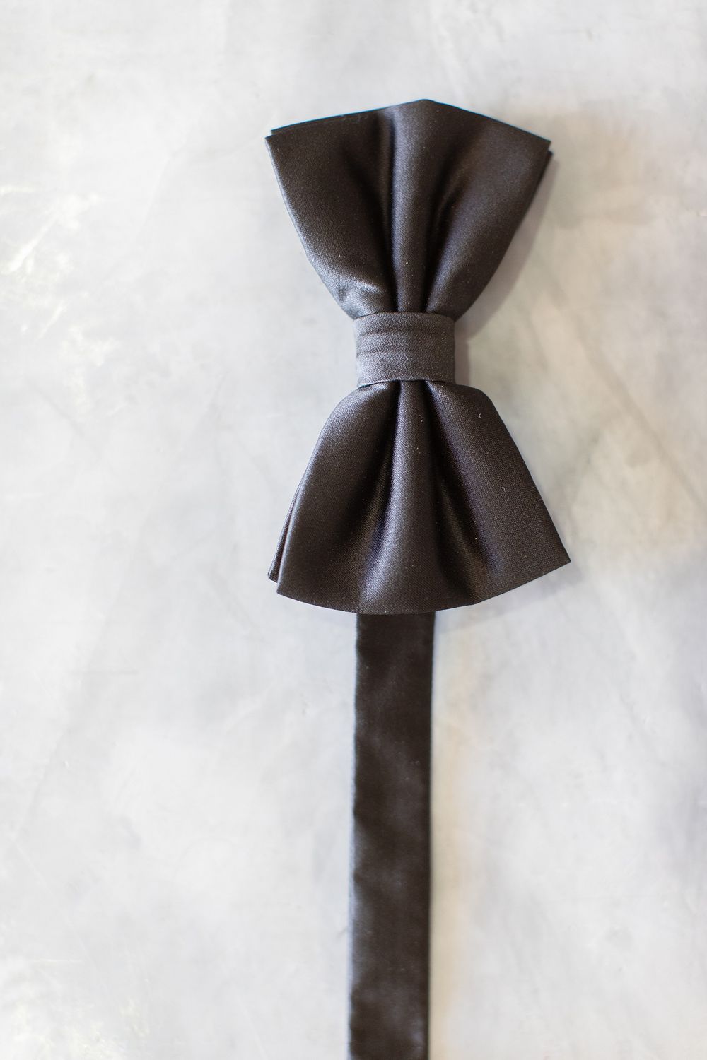 Dark brown satin bow tie laid flat on a marble surface, perfect for formal occasions and black tie events.