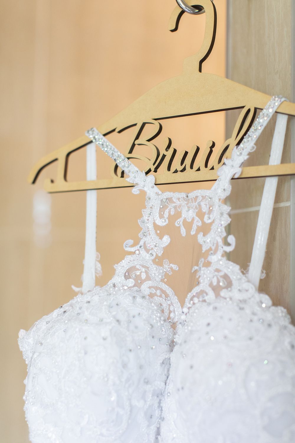 White lace beaded bridal gown hanging on a decorative Bridal hanger, showcasing intricate embroidery and pearl details.