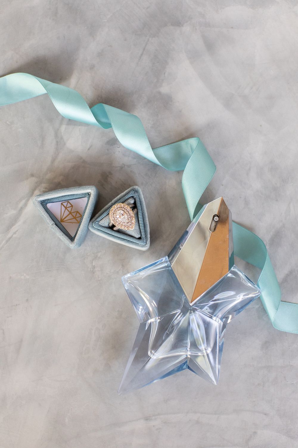 Elegant star-shaped perfume bottle with mint ribbon and triangular jewelry boxes on marble surface.