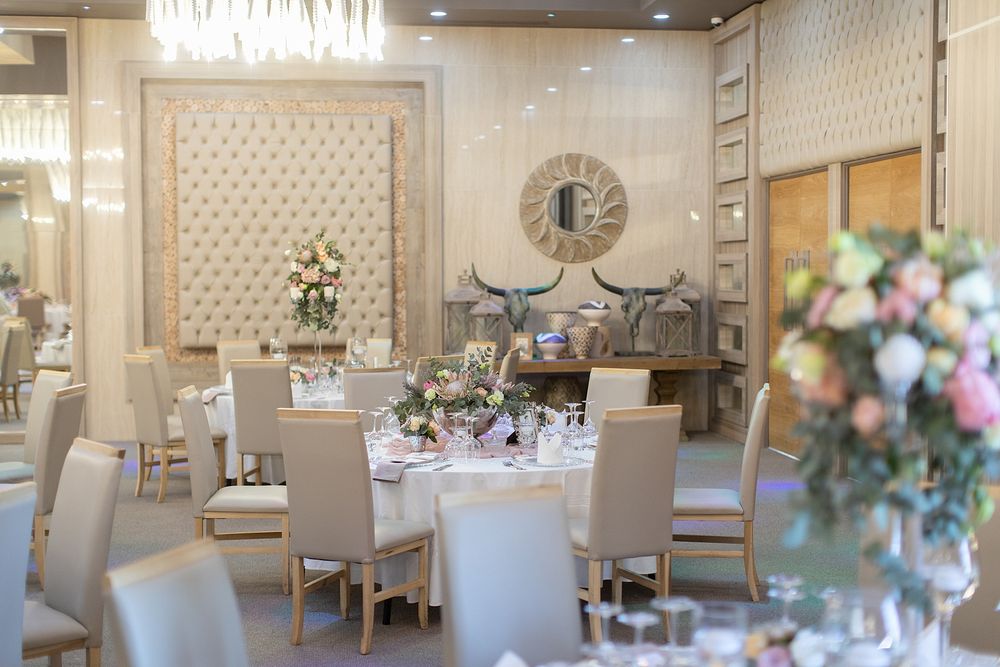 Elegant wedding reception hall with ivory tufted walls, round tables, floral centerpieces, and gold chairs.
