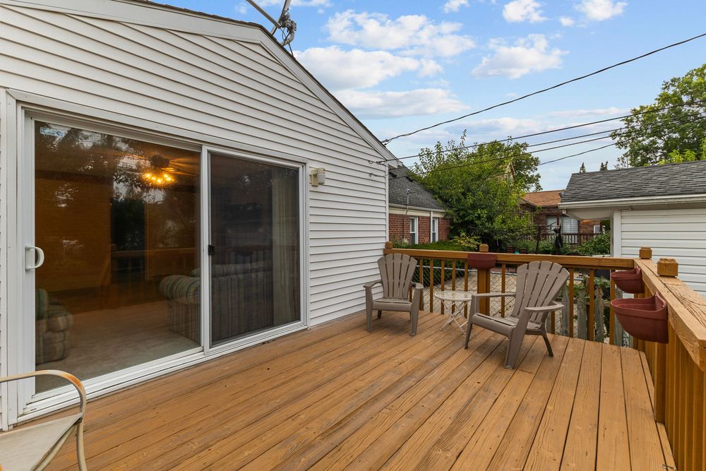 Wooden backyard deck with two chairs, sliding glass door, and white siding on a sunny day.