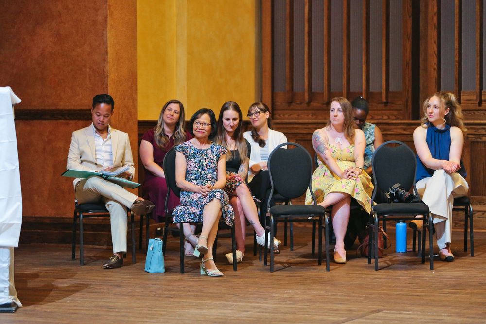 Group of women seated in chairs on a stage during a panel discussion or ceremony in an elegant hall.