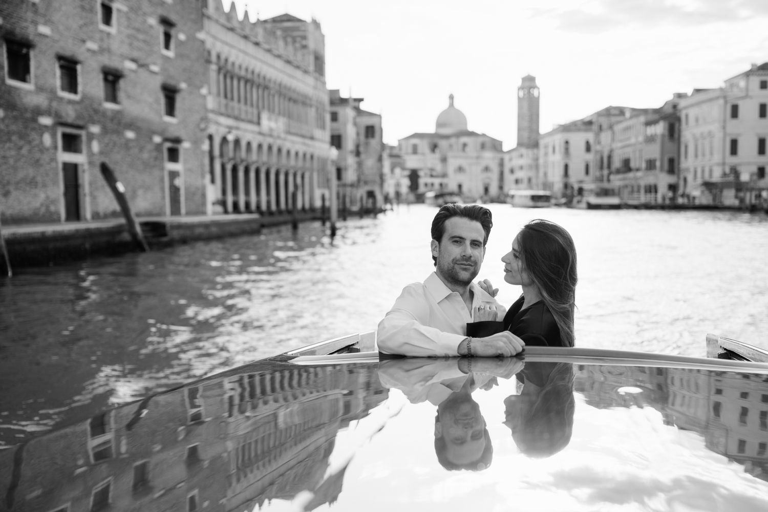 Romantic couple embracing on a gondola in Venice canal with historic buildings in black and white.