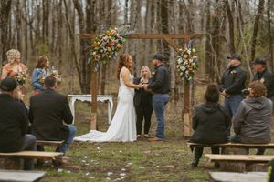 Couple exchanges vows at a rustic outdoor woodland wedding ceremony with floral arch.