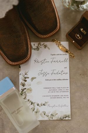 Elegant wedding invitation for Kristen Farrell and Jesse Fedotov with eucalyptus greenery, cowboy boots, perfume, and ring box.