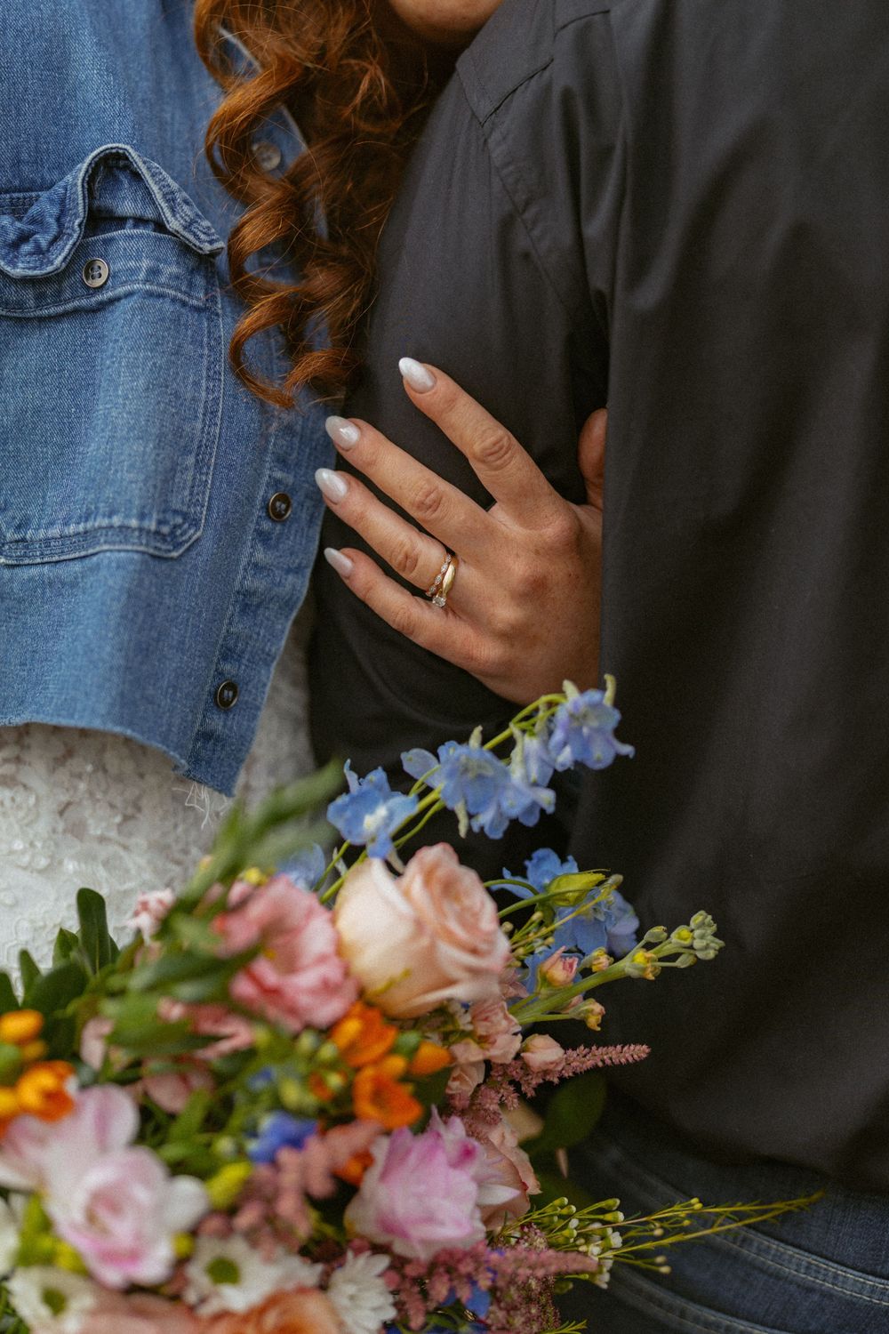 Close-up of a woman's hand with a gold ring holding a colorful flower bouquet during an engagement photo session.