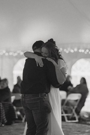 Black and white photo of a couple sharing an emotional first dance embrace at a wedding reception under a tent.