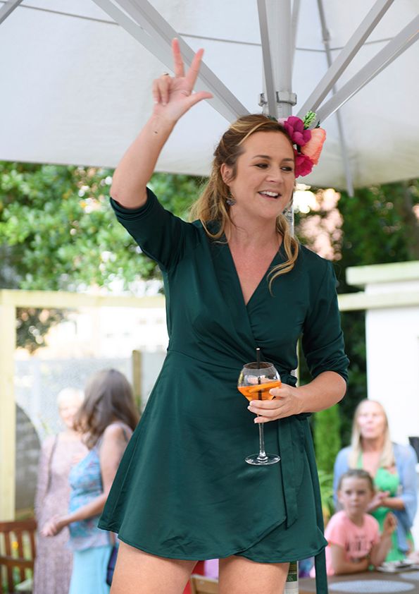 Woman in green dress dances while holding wine glass at outdoor party under white tent.