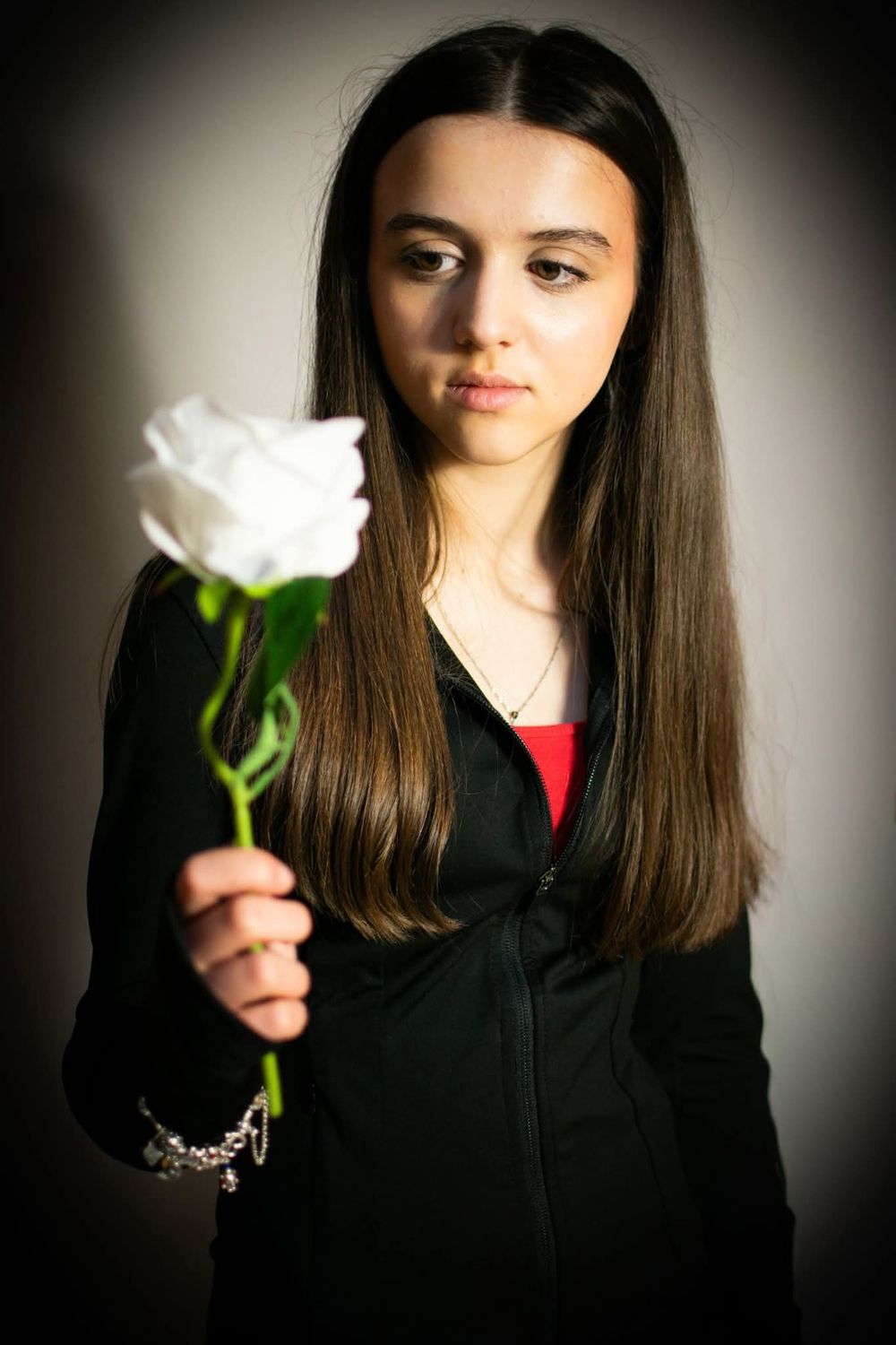 Young teenage girl with long dark hair holding a single white rose toward the camera.