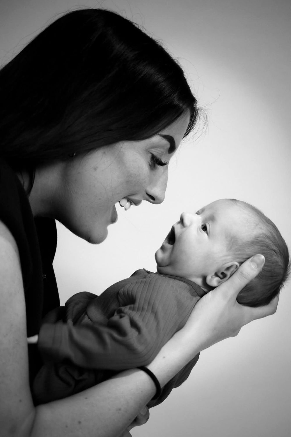 Black and white photo of a smiling mother holding and gazing at her newborn baby.