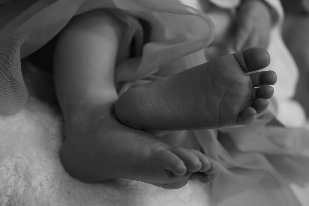 Black and white close-up of tiny newborn baby feet resting on a soft white blanket.