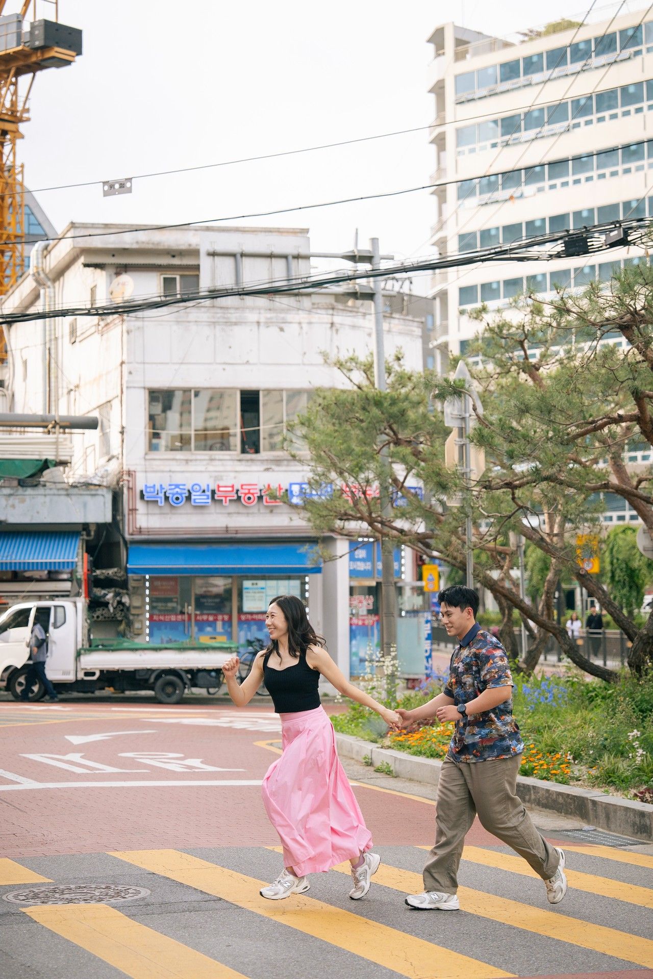 Couple holding hands crossing a zebra crossing on a busy urban street in South Korea.