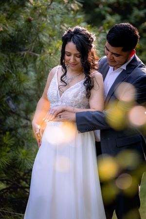 Bride and groom share a tender moment in a lush forest setting, with the groom placing a ring on the bride's finger.