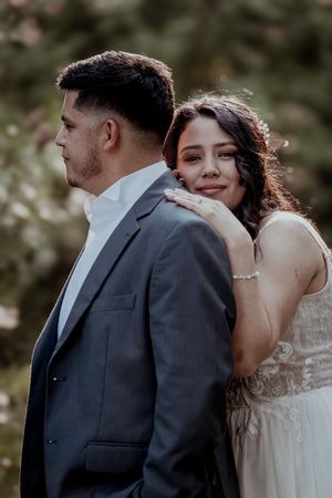 Smiling bride in white dress leans against groom in gray suit during an outdoor wedding photo session.