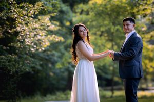 A bride in a white gown and groom in a navy suit hold hands in a lush green garden setting.