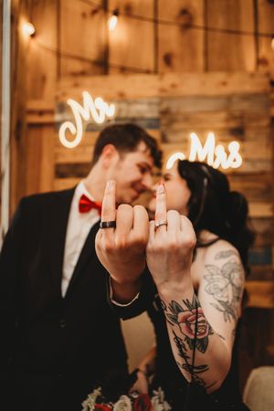 Newlyweds show off wedding rings on middle fingers before Mr. and Mrs. neon signs in rustic barn venue.