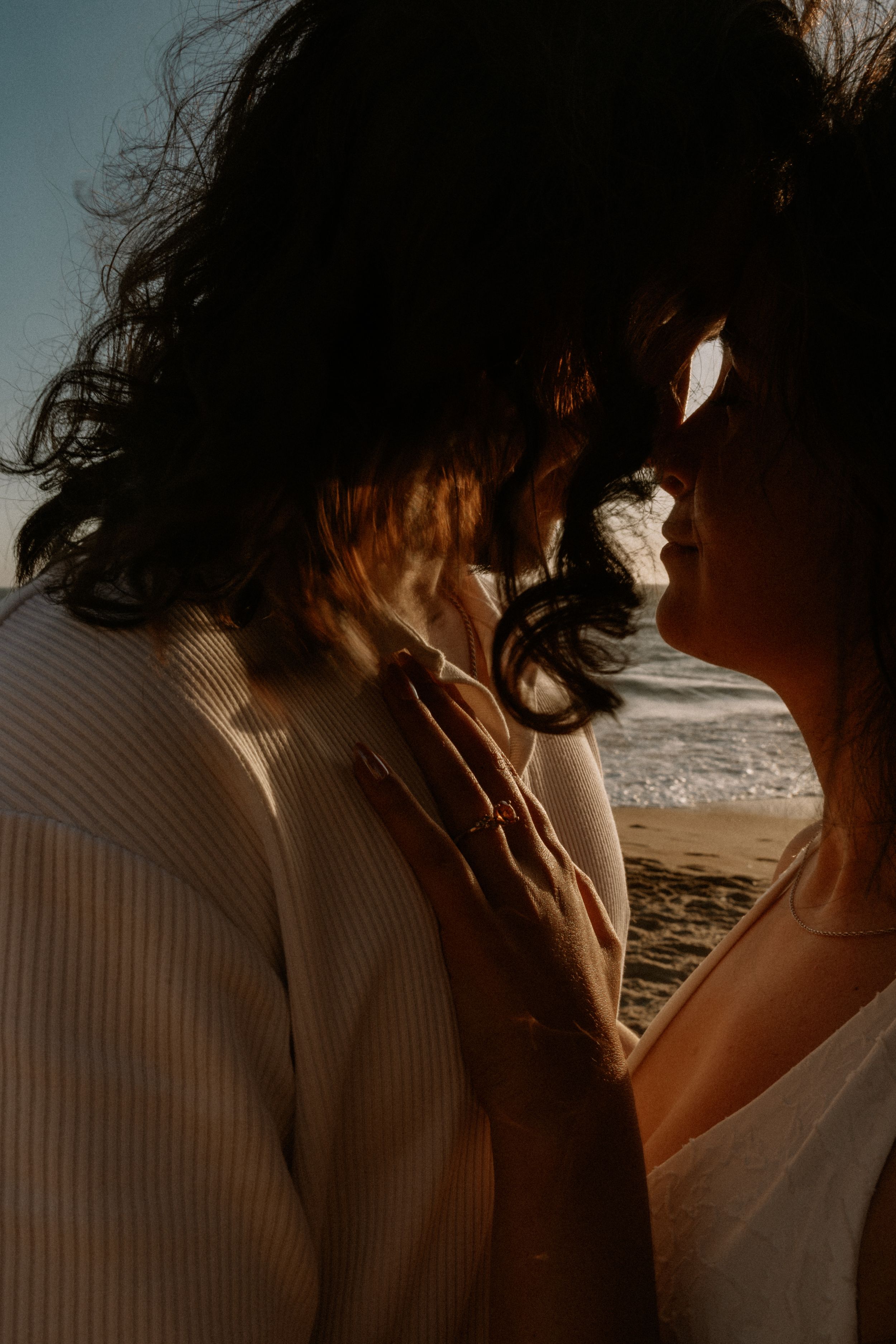Couple sharing a romantic moment on a beach at sunset, silhouetted against ocean waves.