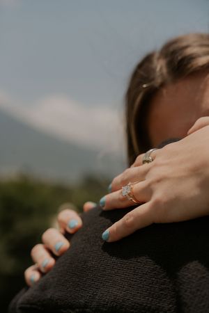 Close-up of a woman's hand with blue nails and a sparkling engagement ring resting on a man's dark jacket.