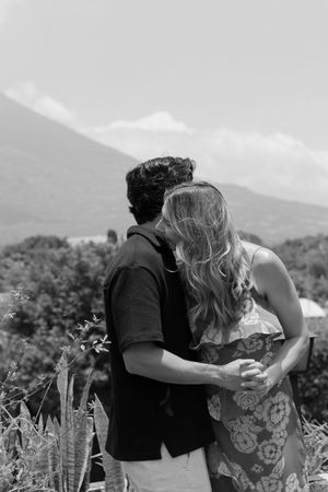 Black and white image of a couple embracing and kissing with a volcanic mountain landscape in the background.
