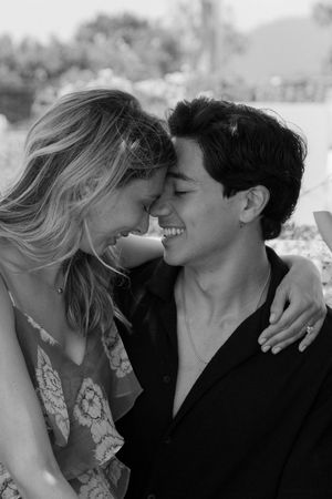 Black and white photo of a smiling couple leaning foreheads together in a romantic outdoor embrace.