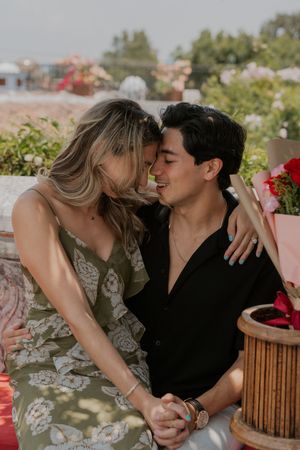 Happy couple sharing a romantic moment, holding hands and smiling in a flower-filled outdoor setting.