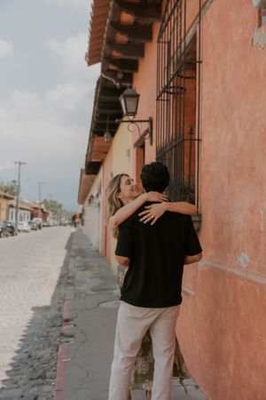 Couple embracing romantically on a cobblestone street beside a colorful terracotta wall in Antigua, Guatemala.