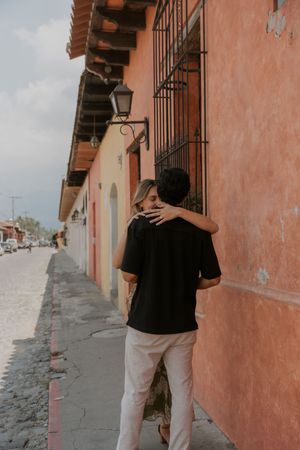 Couple embracing while walking along a colorful colonial street with terracotta buildings.