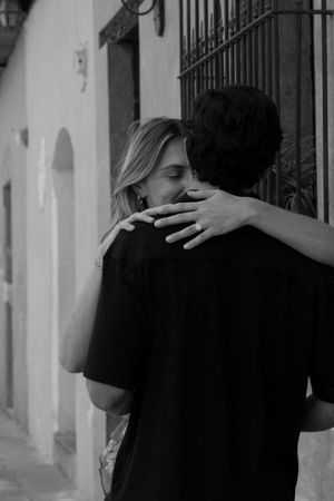 Black and white photo of a couple embracing and kissing on a charming outdoor street.