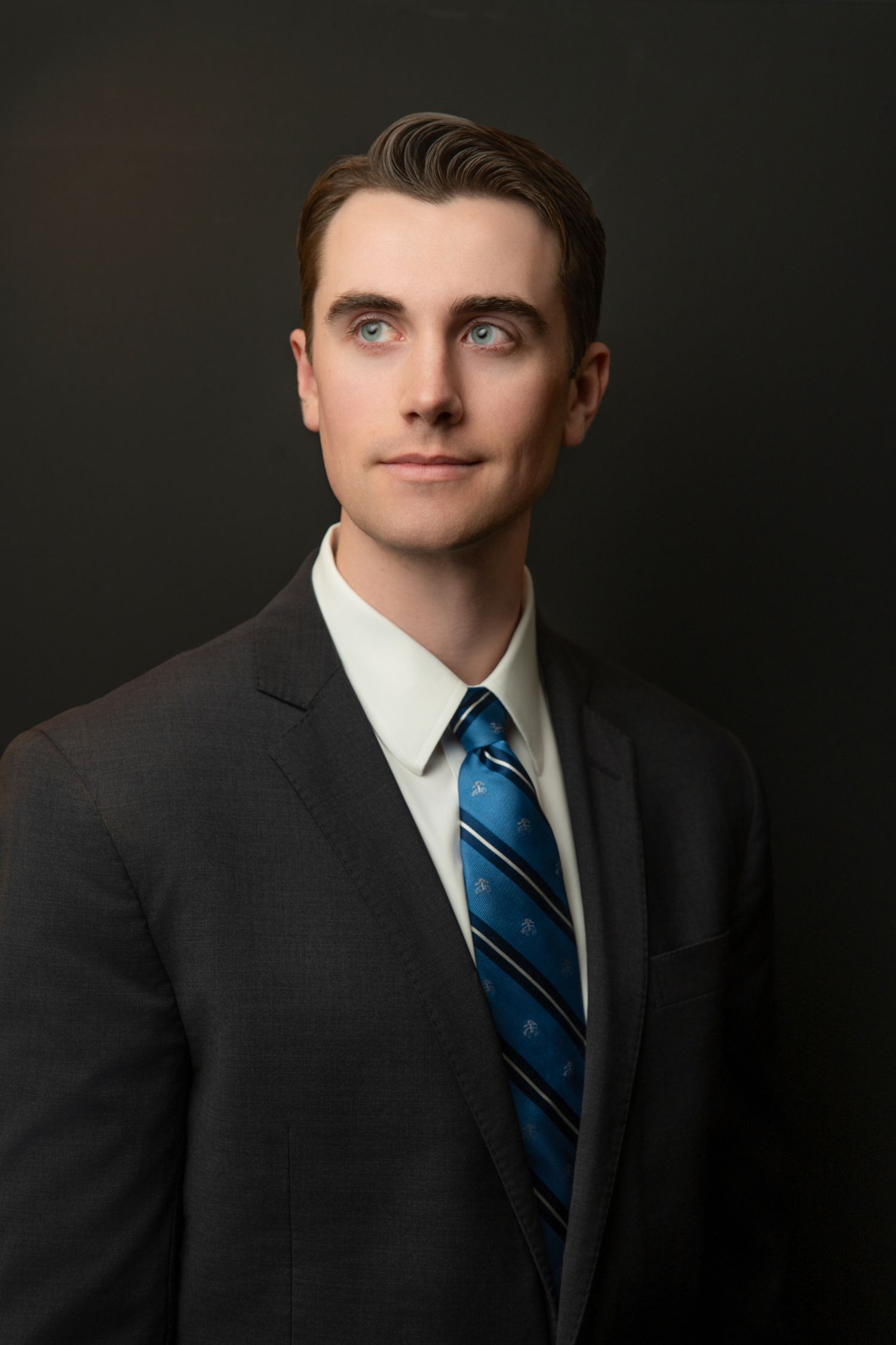Professional headshot of a confident man in a gray suit and red tie against a dark background.