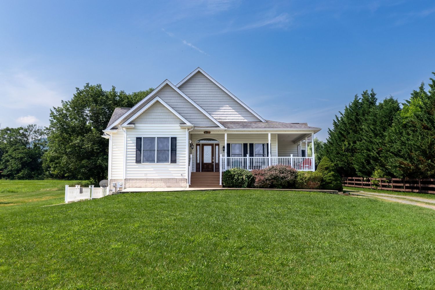 White craftsman home with covered porch, lush green lawn, and mature trees under a bright blue sky.