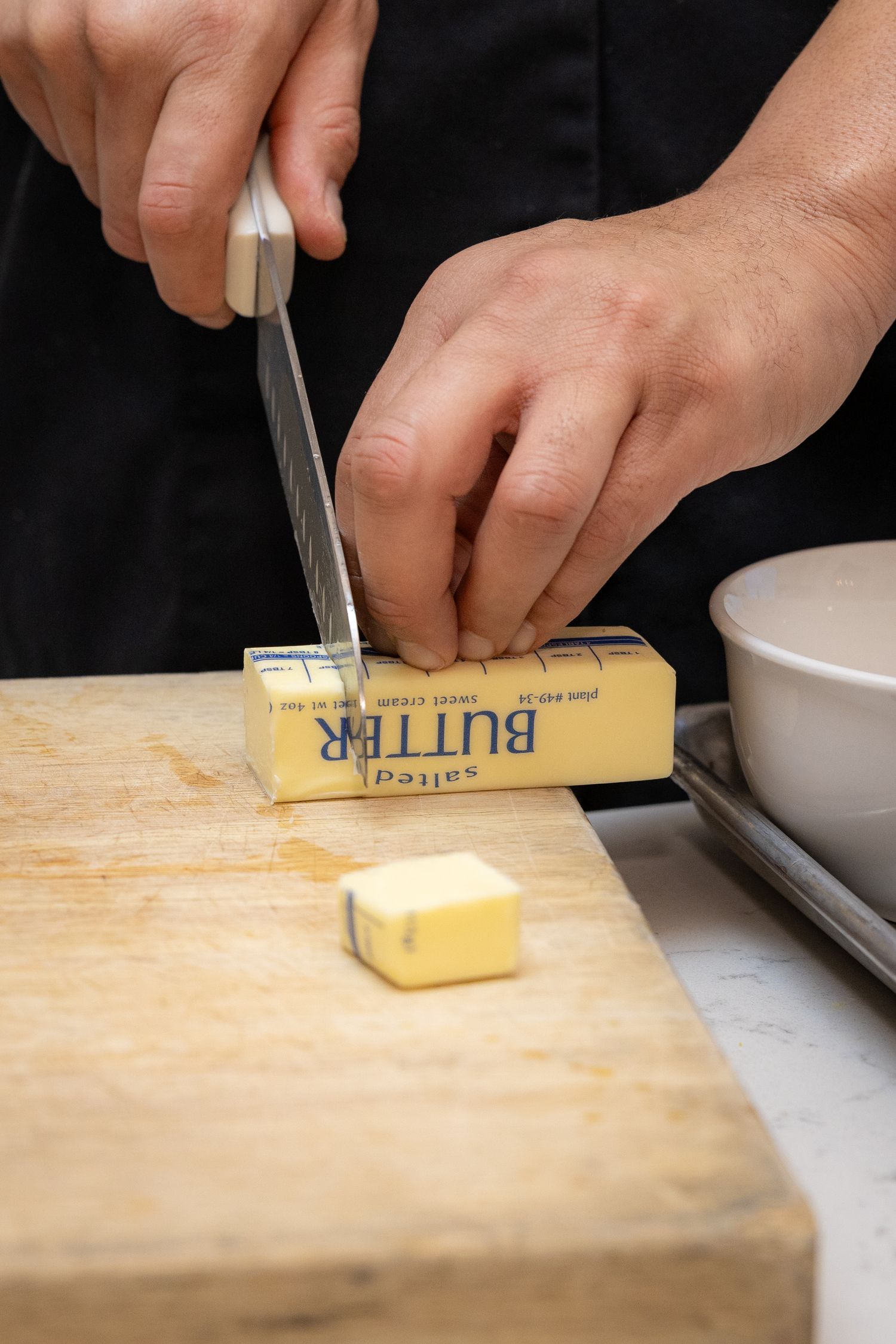 Chef slicing salted butter on a wooden cutting board with a knife in a professional kitchen.
