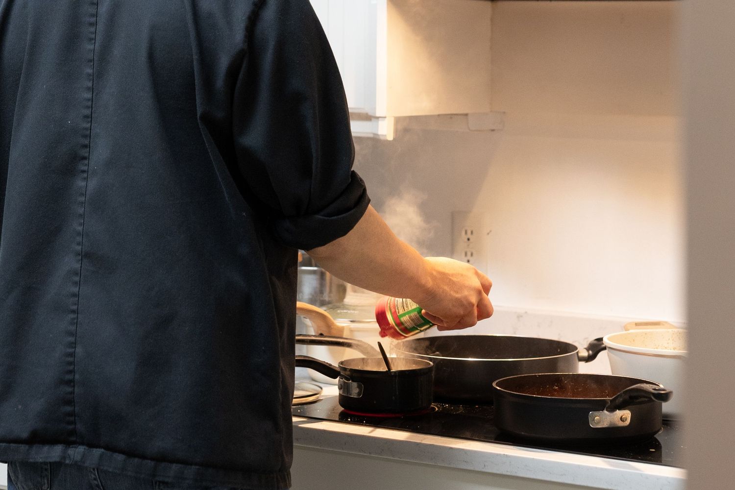 Person cooking on stovetop with two pans, stirring food in a modern kitchen.