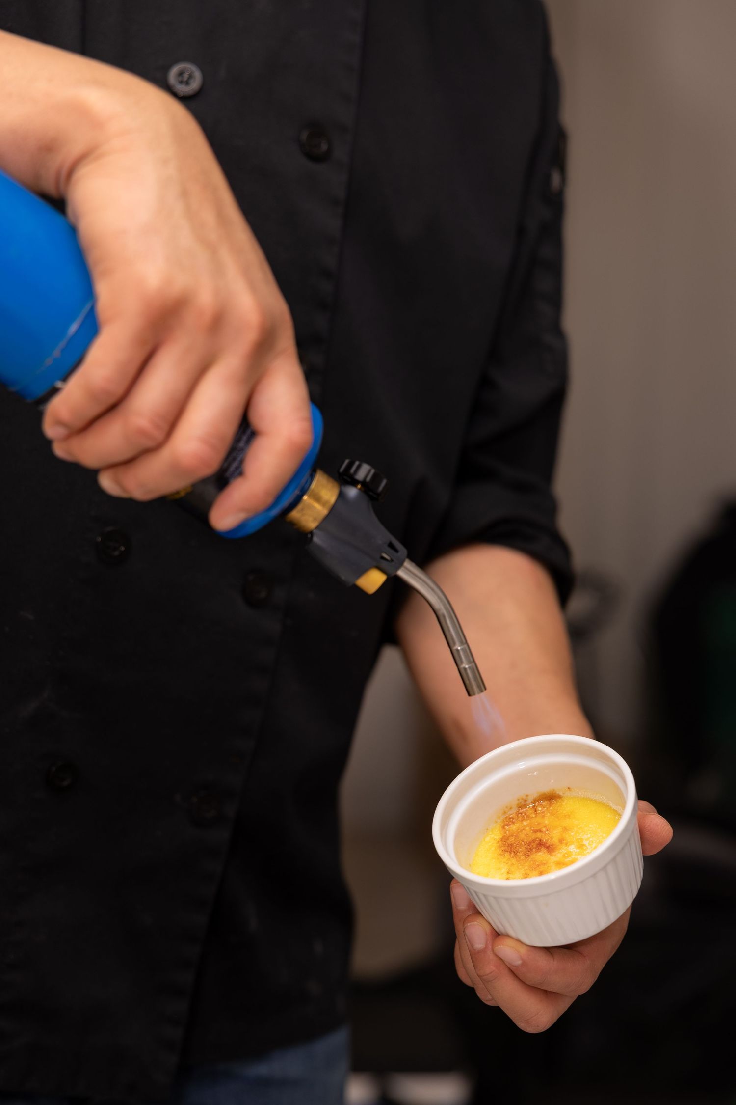 Chef using a culinary torch to caramelize the sugar topping on a classic creme brulee dessert in a white ramekin.