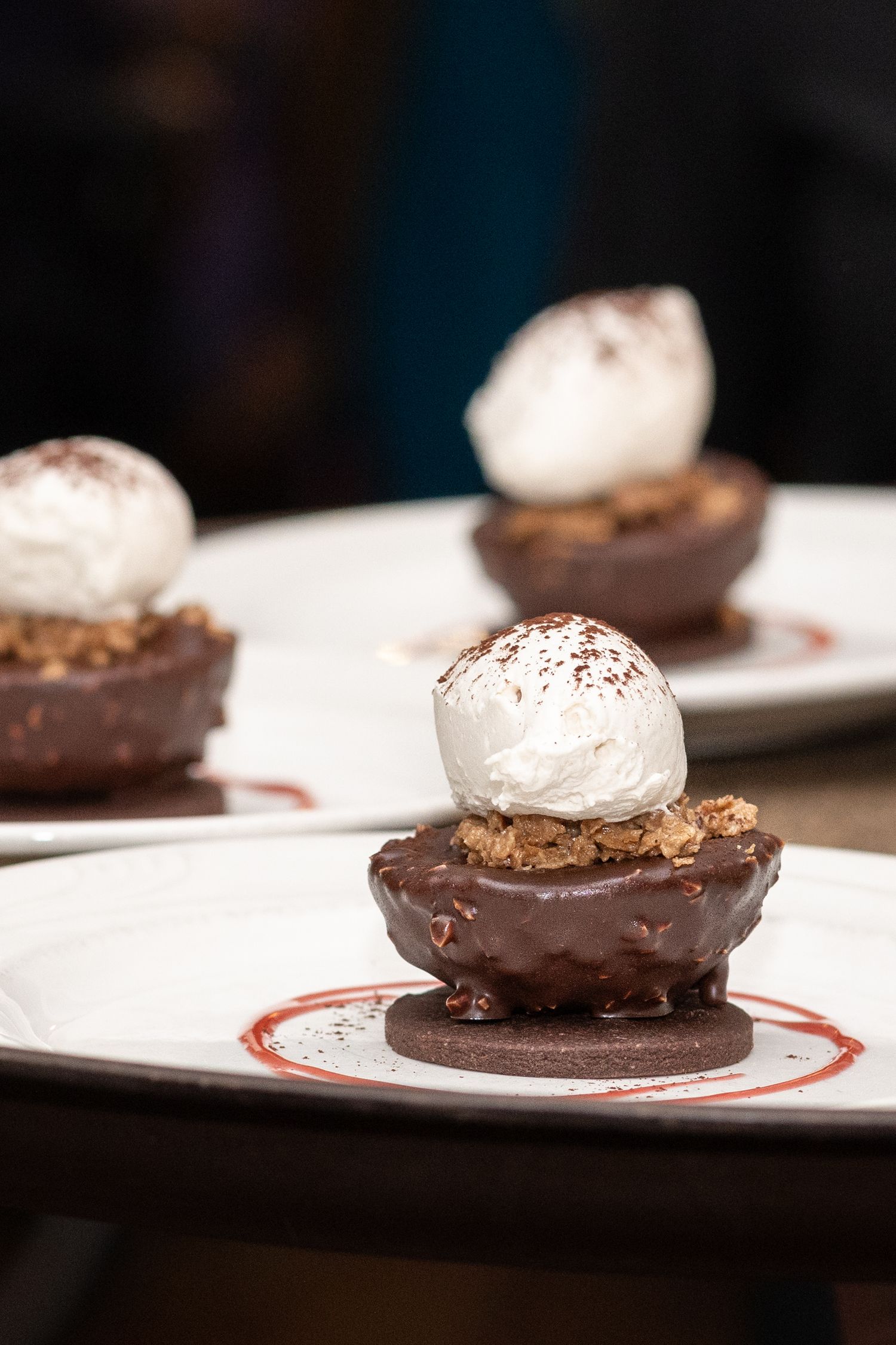 Chocolate tart cups topped with whipped cream and cocoa powder served on white plates.