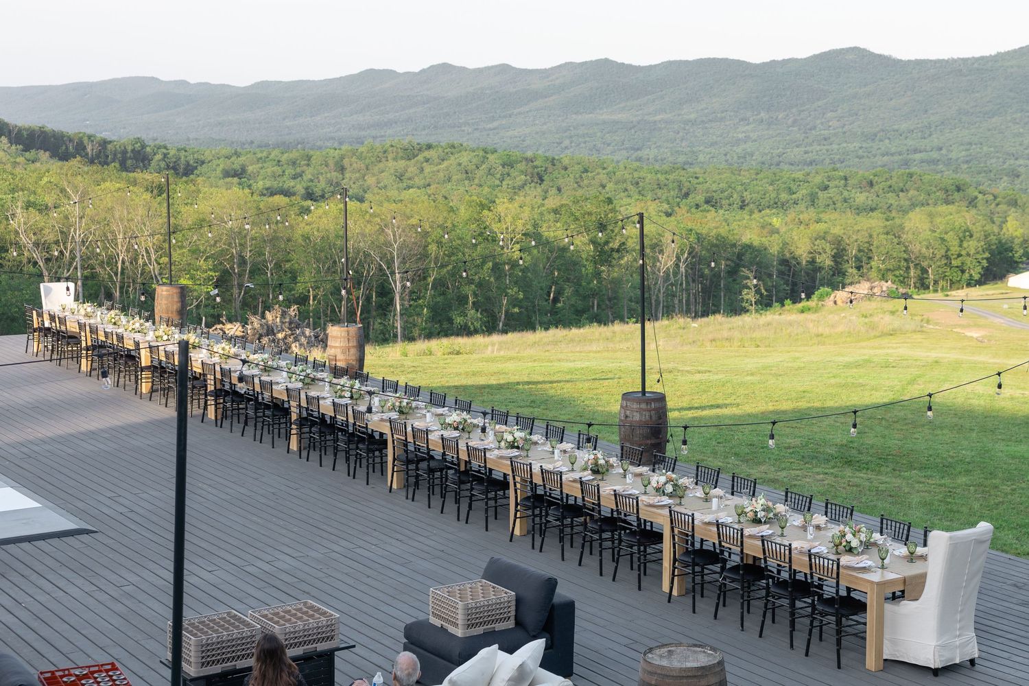 Elegant outdoor wedding reception on a deck with long dining tables overlooking a lush green mountain valley.