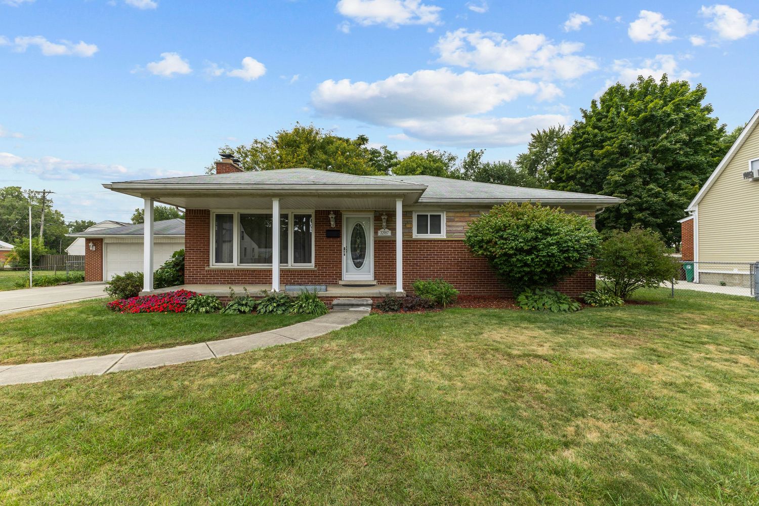 Neat brick ranch home with covered front porch, well-maintained landscaping, and attached garage.