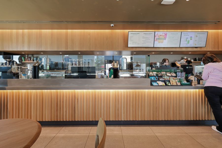 Modern Starbucks counter with warm wood paneling, menu boards, and baristas serving customers in a bright cafe.