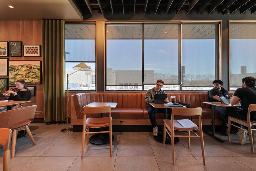 Modern cafe interior with leather booth seating, wooden chairs, and large windows overlooking a city street.