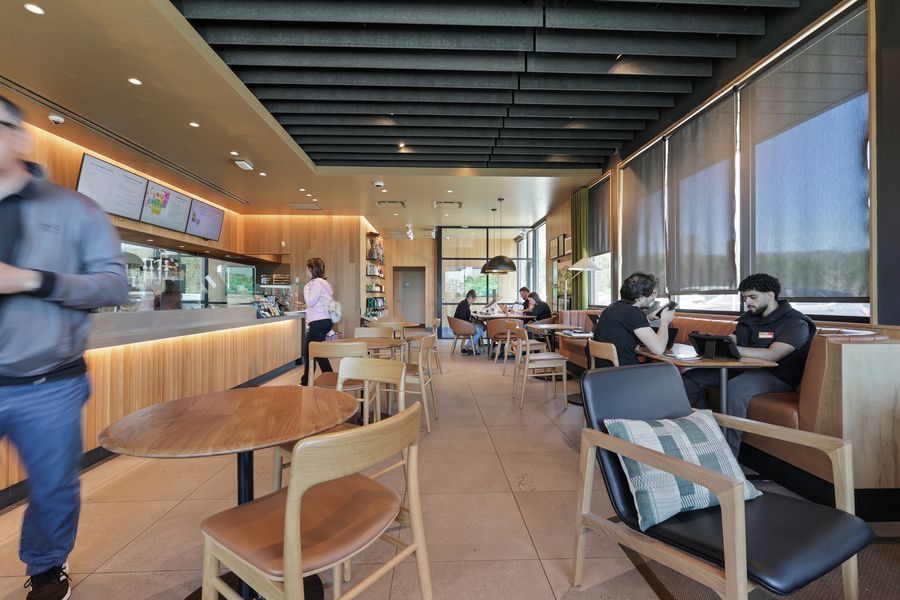 Modern cafe interior with wooden furniture, warm lighting, and customers dining near large windows.